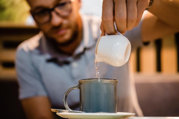 Lateinischer Mann, der in einem Café Wasser in seinen Espressokaffee gibt