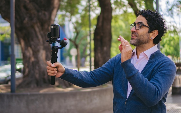 Lateinischer Mann mittleren Alters, der das OK-Zeichen macht, während er sich in einem Stadtpark filmt