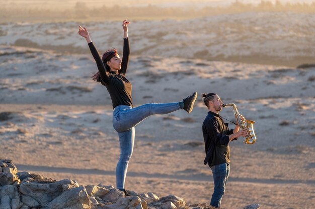 lateinischer musiker spielt saxophon, während lateinische frau bei sonnenuntergang in der wüstenlandschaft tanzt