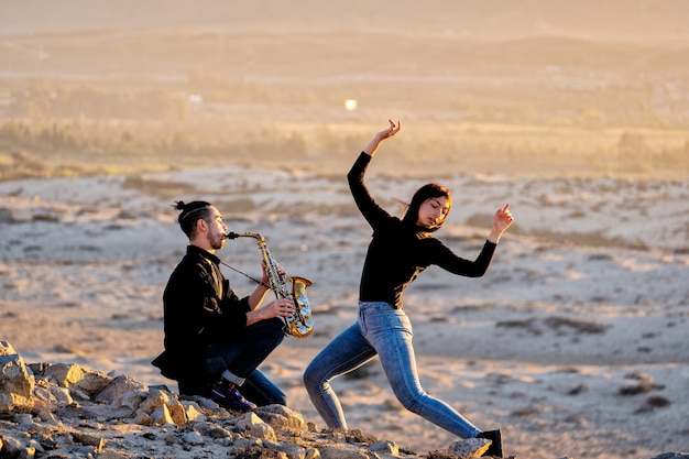 lateinischer musiker spielt saxophon, während lateinische frau in der wüstenlandschaft tanzt