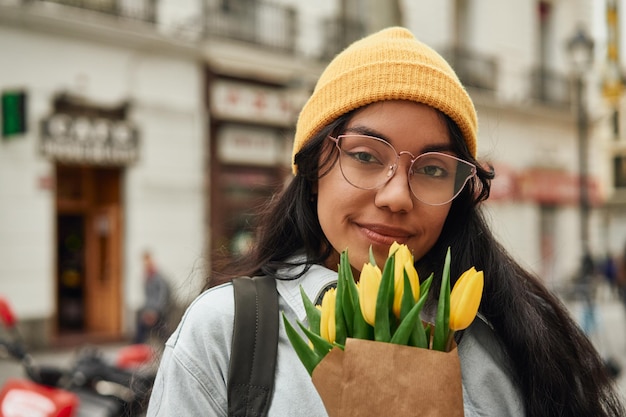 Latina alegre que huele tulipanes soleados en una calle vibrante