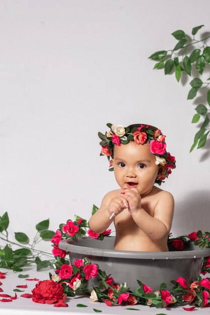 Latina-Baby mit brauner Haut in einem grauen Eimer, umgeben von Blumen und Rosen und rot