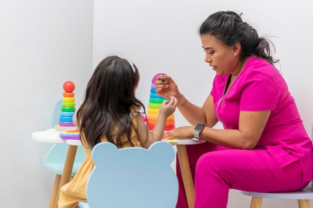Latina-Kinderärztin, die mit einer Patientin sitzt, die an einem Kindertisch in ihrem Büro zeichnet