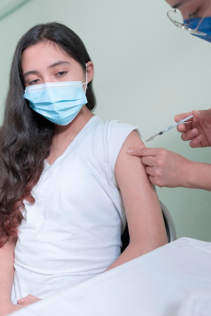 Latina-Krankenschwester injiziert hispanischen weiblichen Teenagern mit einer Spritze Impfstoff in den Arm