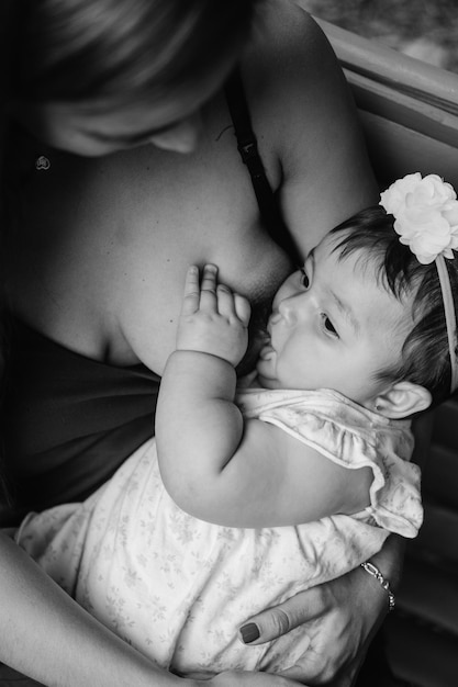 Latina-Mutter, die ihr kleines Mädchen stillt, vertikales Schwarz-Weiß-Foto