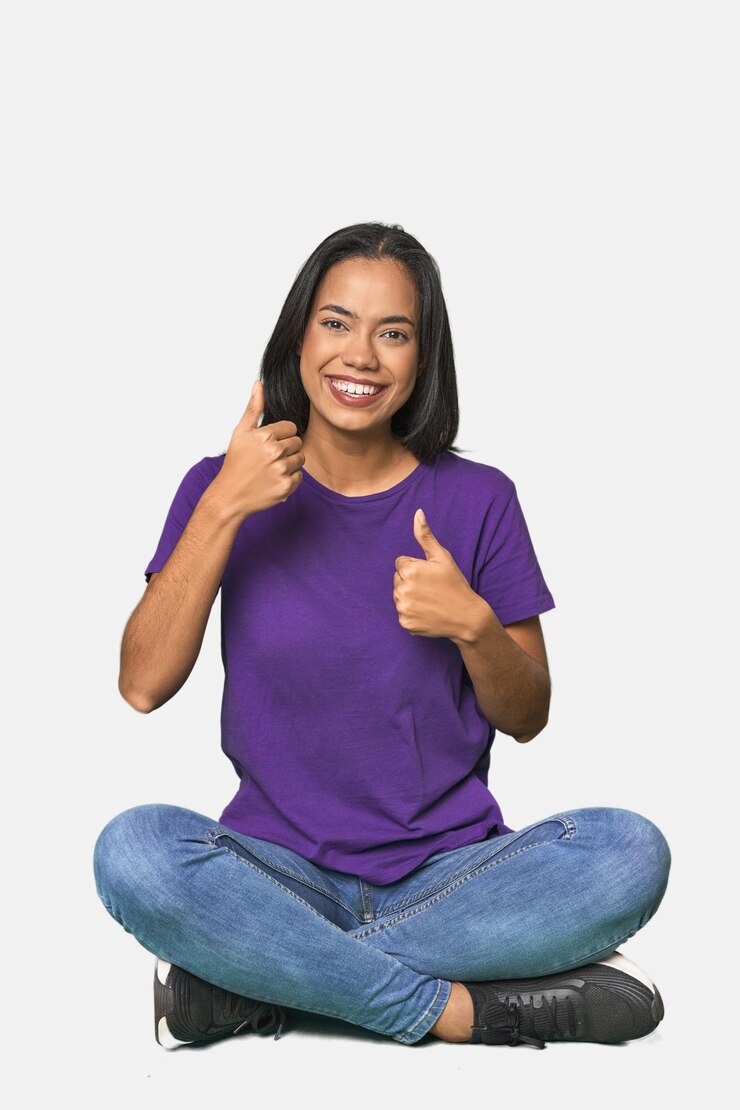Foto latina sentada no chão no estúdio levantando ambos os polegares sorrindo e confiante
