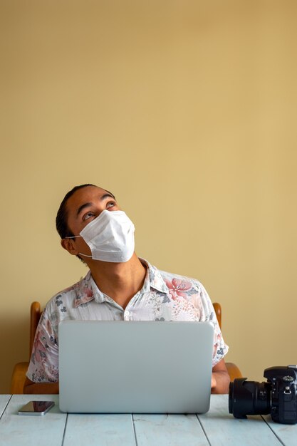 Latino Fotograf mit medizinischer Maske arbeitet zu Hause. Speicherplatz kopieren. Coronavirus-Konzept.