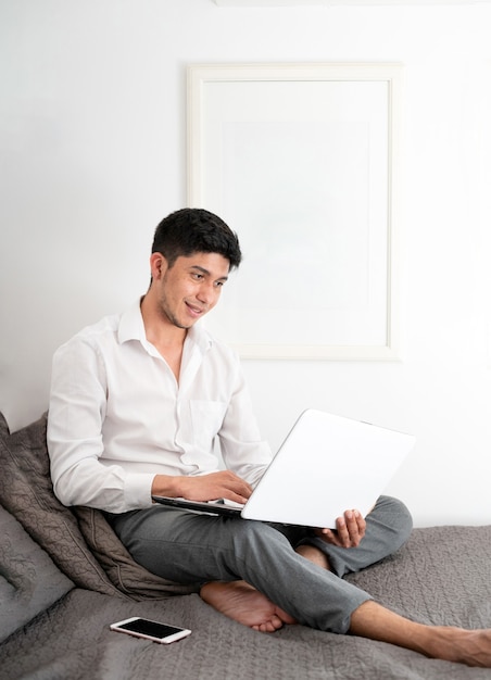 Latino-Mann arbeitet im Bett mit Laptop