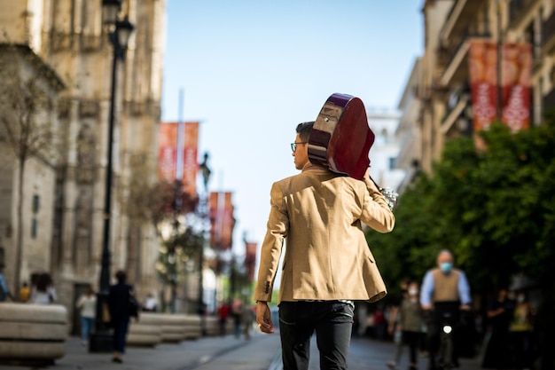 Latino-Mann, der mit einer Gitarre auf der Schulter von hinten eine belebte Straße entlang geht