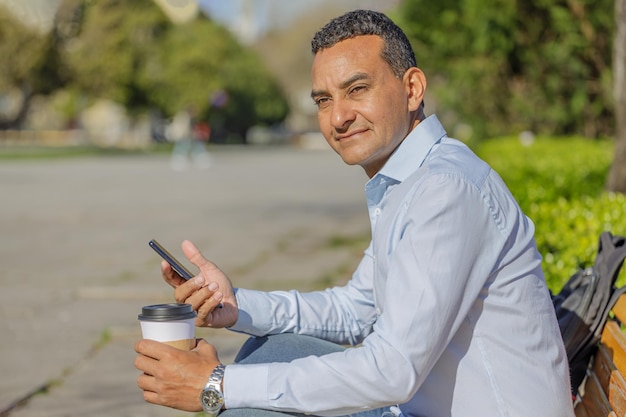 Foto latino-mann macht auf einer öffentlichen parkbank eine pause, um einen kaffee zu trinken