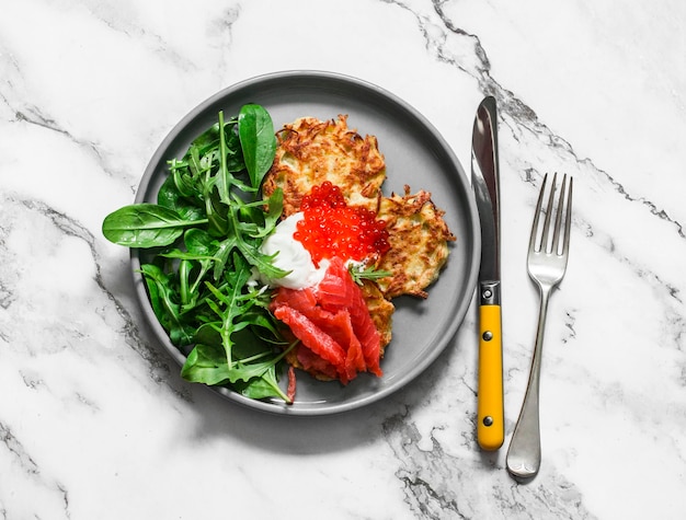 Latkes de batata com iogurte grego de salmão salgado de caviar vermelho e mistura de salada verde em uma vista superior de fundo claro