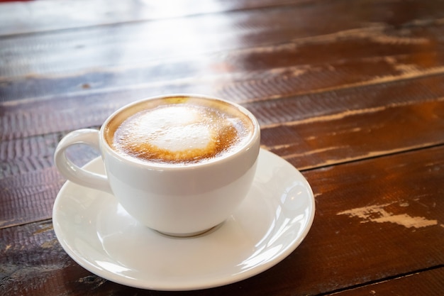 Latte art em forma de coração em uma xícara de café branca na mesa de madeira de um café restaurante