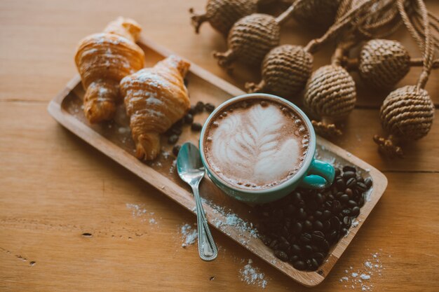 Latte art o capuchino en taza verde con pan y granos de café en la mesa