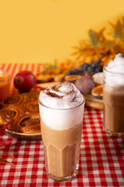 Latte batido con especias de calabaza en vaso Bebida caliente de otoño Cerca de deliciosos pasteles y aperitivos, frutas y queso