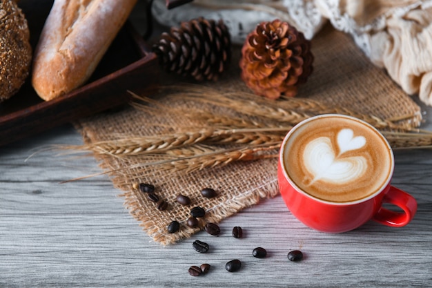 Latte del café del corazón en taza roja con pan.