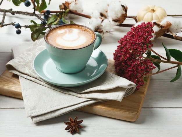 Latte de calabaza y especias. Taza de café azul con espuma cremosa en el escritorio, flores secas de otoño, endrinas y pequeñas calabazas amarillas. Bebidas calientes de otoño, concepto de oferta de temporada