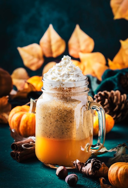 Latte com especiarias de abóbora ou café em frasco de vidro na mesa azul bebida quente de outono ou inverno em cenário de mesa natural festivo com folhas de laranja especiarias pequenas abóboras pinhas