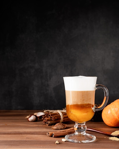 Latte de especiarias de abóbora em uma caneca de vidro com canela e gengibre