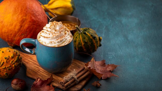 Latte de especias de calabaza en una taza azul con crema batida, canela. Fondo azul decorado hojas de otoño, calabaza.