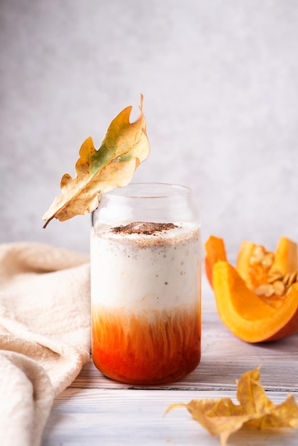 Latte con especias de calabaza en vidrio sobre mesa de madera blanca, bebida de café de otoño con crema batida.