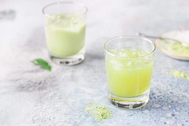 Latte helado verde Matcha en vasos con polvo de matcha sobre fondo claro.