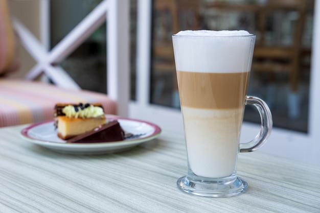 Latte-Kaffee in einem Glasbecher und ein Kuchen steht auf dem Tisch in einem Café. Sommerterrasse.