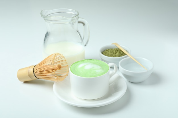 Latte matcha y accesorios para hacer sobre fondo blanco.