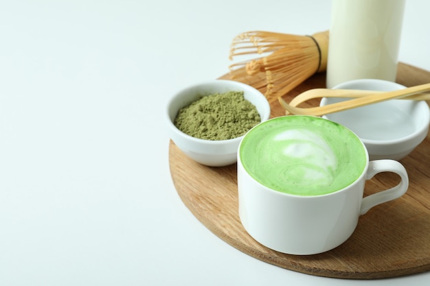 Latte matcha y accesorios para hacer sobre fondo blanco.