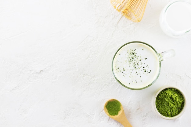 Latte matcha con leche de coco en una taza de vidrio con polvo y batidor