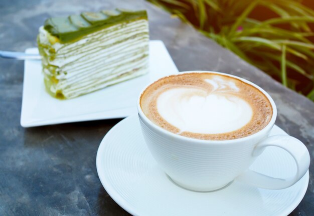 Latte oder Cappuccino-Kaffee in der weißen Tasse mit grünem Teekuchen auf Tisch