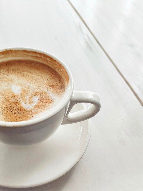 Foto latte oder cappuccino mit schaumiger schaumkaffeetasse draufsicht auf weißem holztisch im café vertikales foto draufsicht