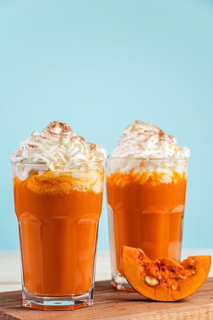 Latte picante de calabaza con crema batida sobre fondo azul Dos vasos de bebida caliente de otoño