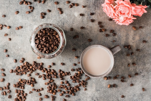 Latte en un tarro de cerámica con granos de café y rosas en la mesa Vista superior