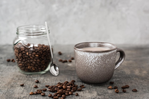 Latte en una taza de cerámica y un frasco con granos de café sobre la mesa Tiempo para un descanso y relajación