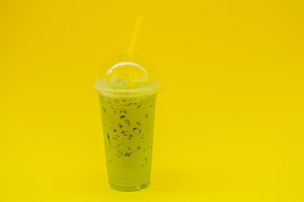 Latte de té verde con hielo en vaso de plástico y paja en mano femenina con manicura amarilla sobre fondo amarillo Té de latte matcha helado casero con leche para llevar