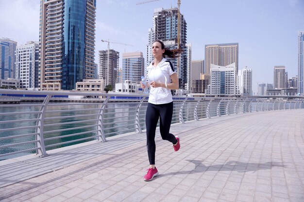 Laufen im Stadtpark. Frau Läufer draußen Joggen am Morgen mit Dubai urbane Szene im Hintergrund