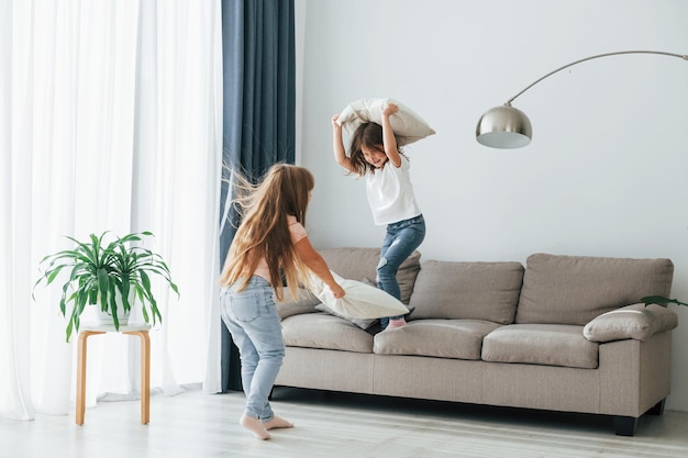 Laufen mit Kissen Kinder, die sich tagsüber gemeinsam im Wohnzimmer amüsieren