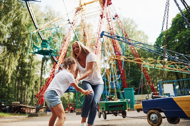 Foto laufen und spielen. fröhliches kleines mädchen, ihre mutter, haben eine gute zeit im park zusammen in der nähe von attraktionen.