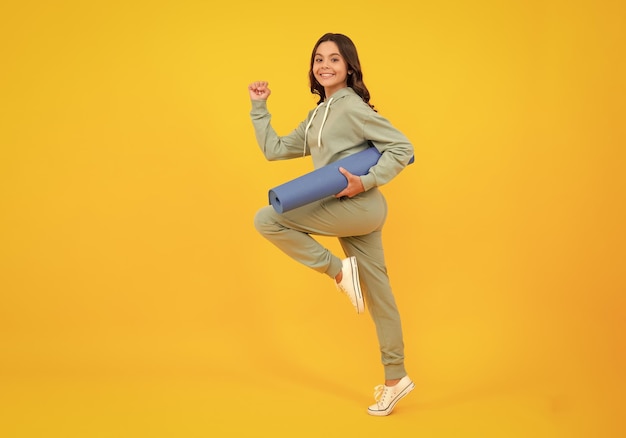 Laufen und springen Mädchen Teenager im Trainingsanzug Glückliches süßes Kind in einem gelben Sportanzug gelber Hintergrund