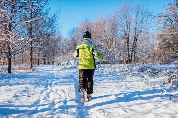 Laufende Athletenfrau, die in Winterwald sprintet. Draußen trainieren bei kaltem Schnee.