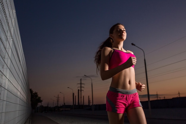 Laufende Frau. Läufer, der abends joggt. Weibliches Eignungsmodelltraining draußen im Sonnenunterganghimmelhintergrund.