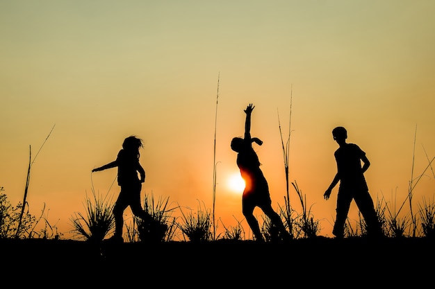 Laufende Gruppe von Kindern läuft auf der Wiese, Sonnenuntergang, Silhouette