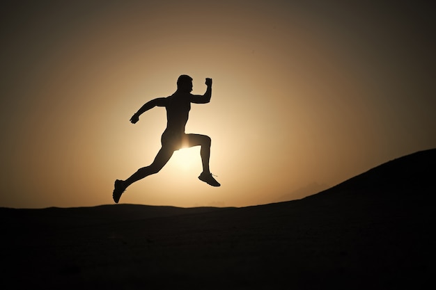 Laufende Silhouette des Mannes auf Sonnenunterganghintergrund, junger kaukasischer Lauf im Berg