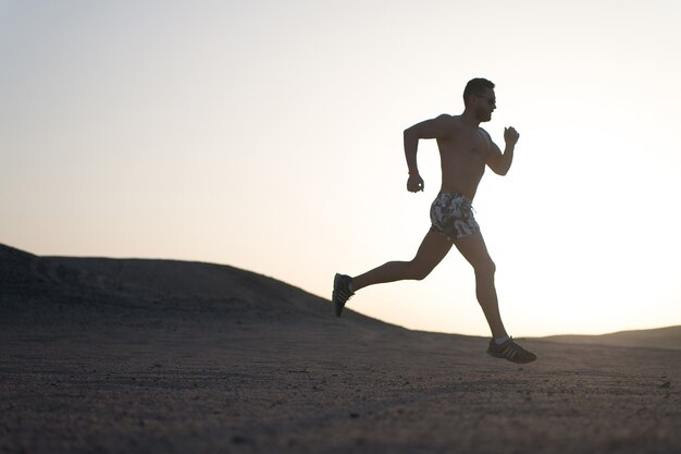 Laufende Silhouette des Mannes auf Sonnenunterganghintergrund, junger kaukasischer Lauf im Berg