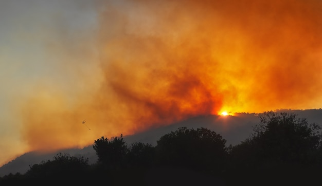 Lauffeuer auf einem Berghang bei Sonnenuntergang mit dramatischem rotem Himmel und starkem Rauch