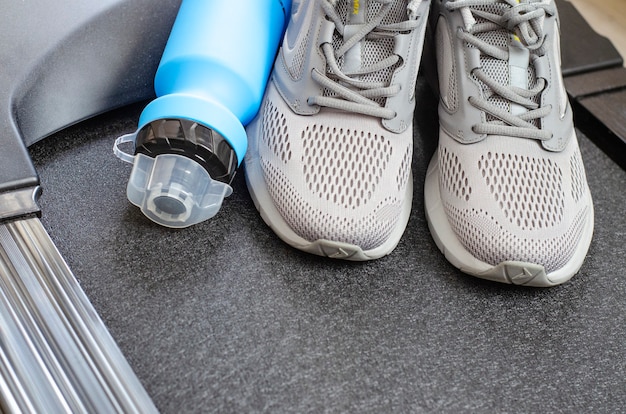 Laufstrecke mit Turnschuhen und einer Flasche Wasser auf schwarzem Hintergrund. Übungsgeräte für die Gesundheit. Studiofoto.