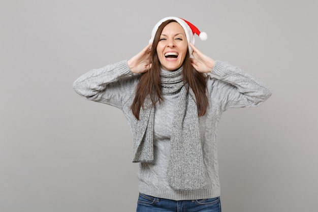 Laughing Merry Santa girl in gray sweater scarf Christmas hat puso las manos en la cabeza aislada sobre fondo gris, retrato de estudio. Feliz año nuevo 2019 celebración concepto de fiesta navideña. Simulacros de espacio de copia.