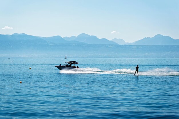 Lausanne, Schweiz - 26. August 2016: Motorboot mit Menschen an Bord und Mann Wakesurfen am Genfer See in Ouchy in Lausanne, Schweiz.