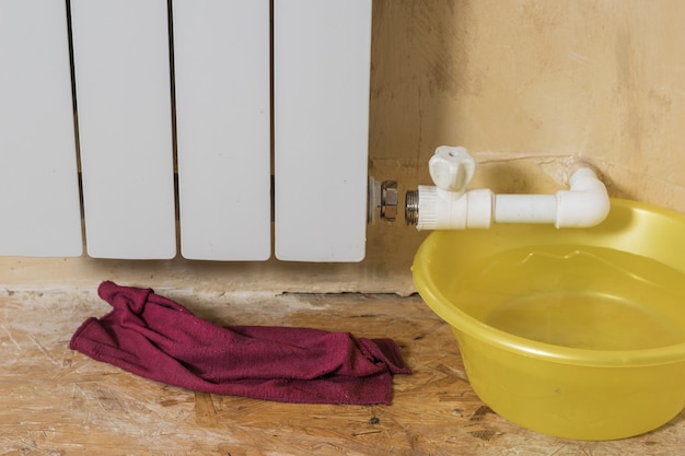 Lavabo amarillo cerca de un radiador con fugas. Accidente del sistema de calefacción de una casa particular. Radiador de calefacción.