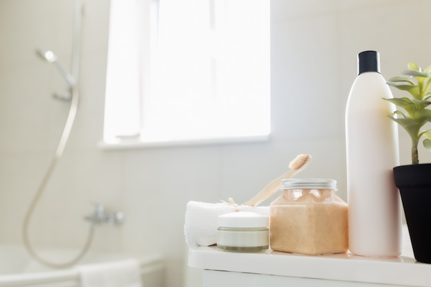 Lavabo y ducha en baño blanco con accesorios de baño. Concepto de limpieza del hotel. Concepto de hogar. Champú, exfoliante corporal, crema, cepillo de dientes, toalla. Luz de ventana.